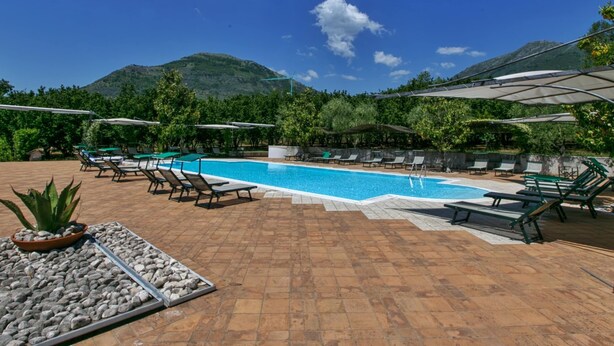 A pool area with lounge chairs and umbrellas, surrounded by greenery and a mountain in the background. - Holiday Home in San Cipriano With Pool (San Cipriano Picentino)