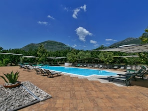 A pool area with lounge chairs and umbrellas, surrounded by greenery and a mountain in the background. - Holiday Home in San Cipriano With Pool (San Cipriano Picentino)
