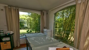 A massage table with towels and a rolled-up towel, a small table with a phone and towels, and large windows with curtains. - Holiday Home in San Cipriano With Pool (San Cipriano Picentino)