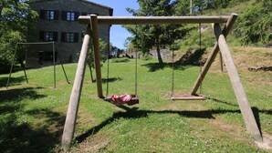 A wooden swing set in a grassy area with a stone building in the background. - Belvilla by OYO Eolo (Apecchio)