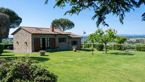 A stone house with a tiled roof, surrounded by a well-maintained lawn and trees.