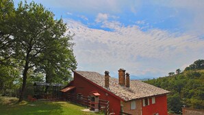 Ein rotes Haus mit Ziegeldach, einer Holzterrasse und einem großen Baum im Vordergrund.