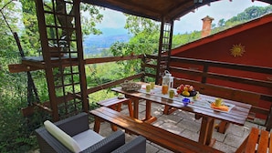 Eine Terrasse im Freien mit einem Holztisch und -stühlen, umgeben von viel Grün und einer schönen Aussicht.