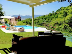 A poolside area with a covered patio, lounge chairs, and a view of a mountainous landscape.