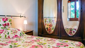 A bedroom with a floral bedspread, a bedside lamp, and a large mirror with a floral curtain. - Belvilla by OYO Villa Nicola (Ricadi)