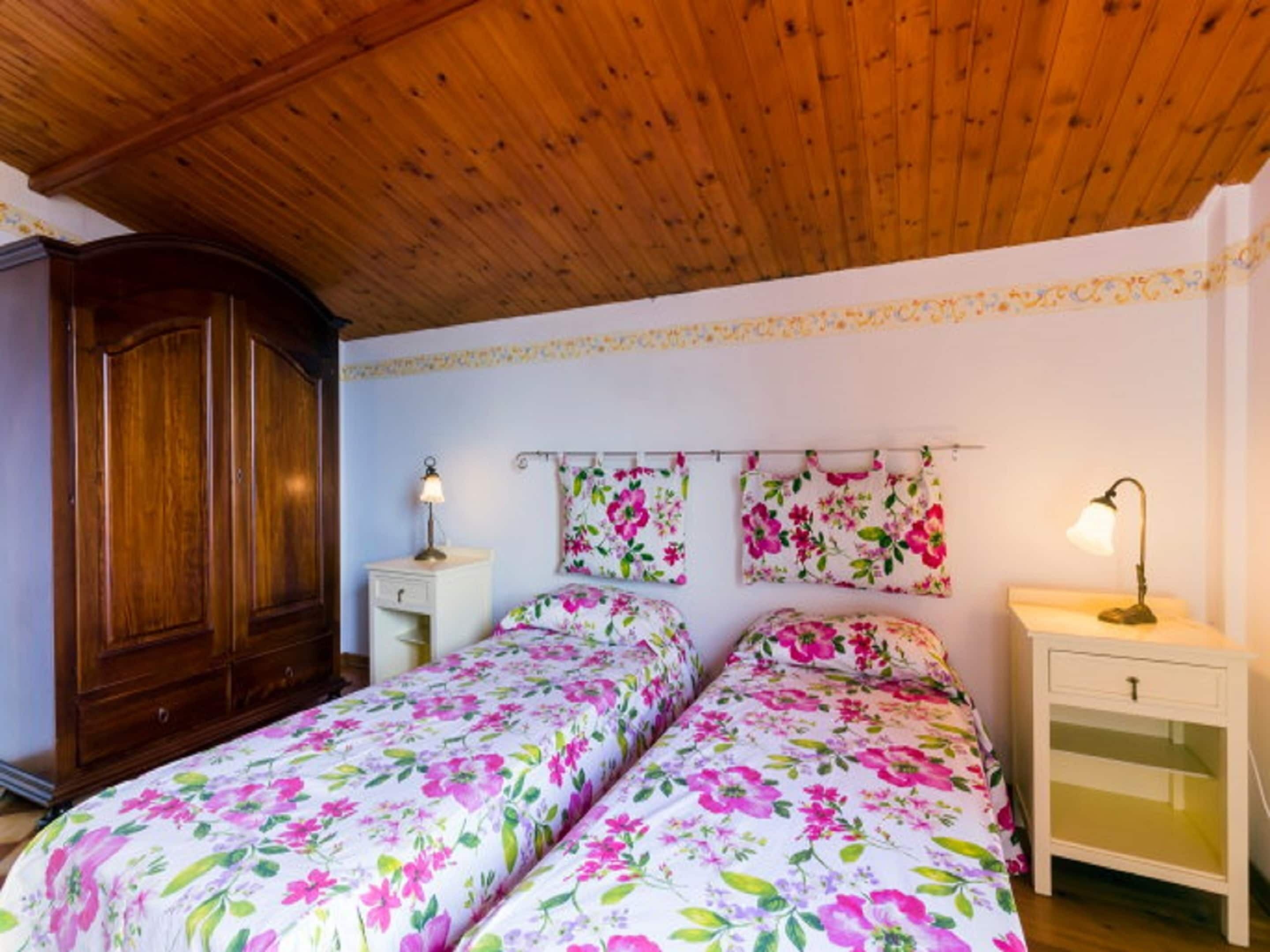 A bedroom with two beds, wooden wardrobe, and a nightstand with a lamp.