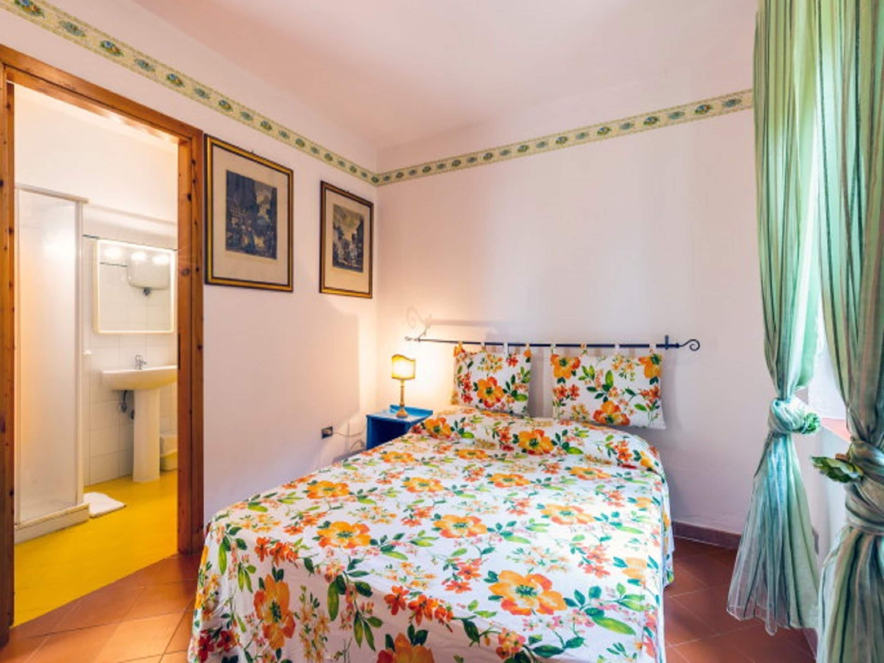 Un dormitorio con colcha estampada, una mesita de noche con lámpara y una puerta que da al baño.