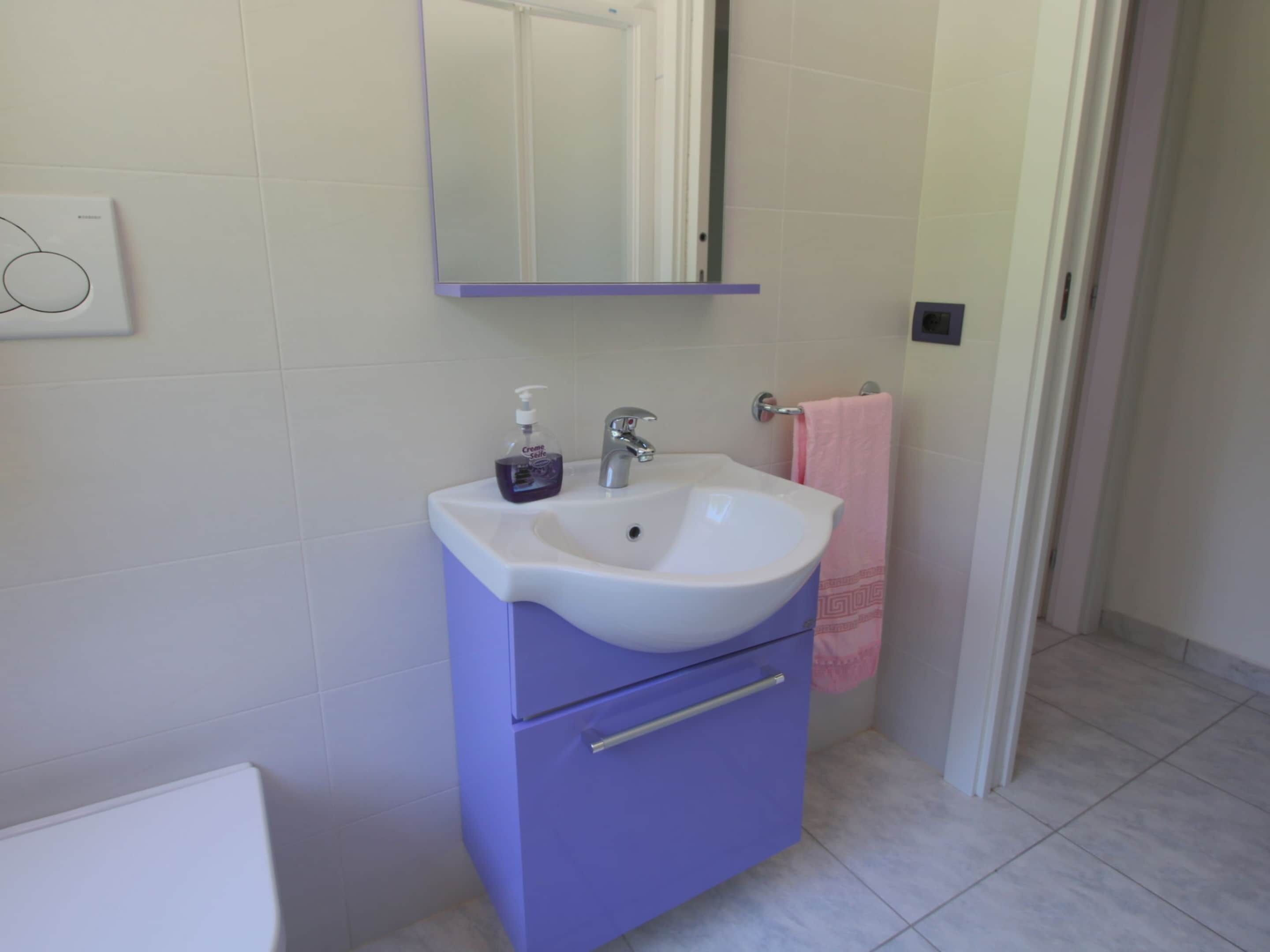 A bathroom with a white sink, purple cabinet, and a mirror above it.