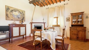 A dining area with a wooden table, chairs, a chandelier, a fireplace, and a cabinet. - Holiday Home in Cortona (Cortona)