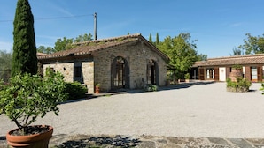 A stone building with a tiled roof, a gravel driveway, and a potted plant in the foreground. - Holiday Home in Cortona (Cortona)