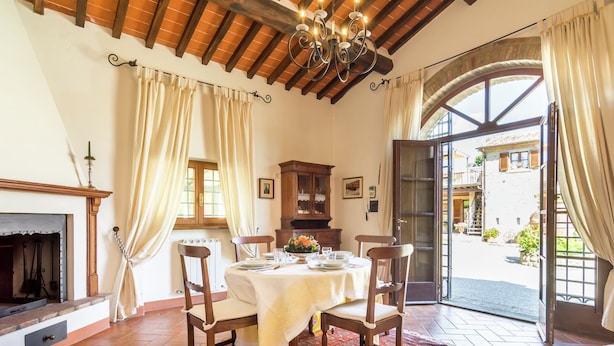 A dining area with a table set for four, wooden chairs, a patterned rug, a fireplace, and a view of the outside. - Holiday Home in Cortona (Cortona)