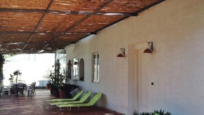 A covered patio area with a tiled floor, green lounge chairs, potted plants, and a white wall with windows and wall-mounted lights. - Cozy Holiday Home in Trecase With Balcony - Casa per Ferie (Trecase)