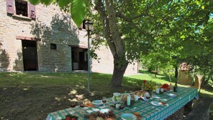 An outdoor dining table set up in a garden with stone buildings in the background. - Farmhouse in Apecchio With Pool (Apecchio)