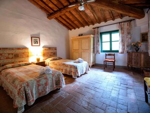 Une chambre avec deux lits, un plafond en bois, une fenêtre avec des rideaux et une chaise.