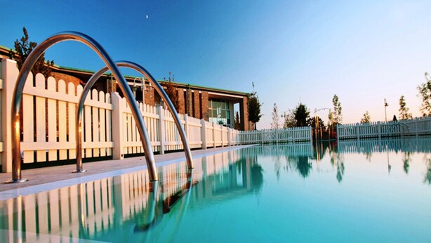 Una piscina con una escalera metálica y una valla blanca al fondo.