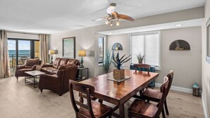 A spacious living room with a wooden dining table, leather sofas, and a ceiling fan.