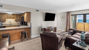 A modern kitchen with a bar area, a flat-screen TV, and a seating area with a view of the ocean.