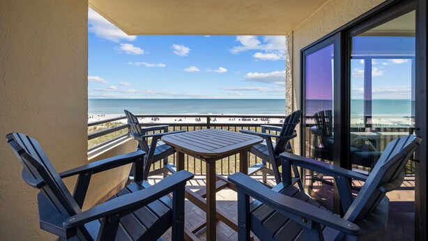 Een balkon met een tafel en stoelen, met uitzicht op een strand en een heldere lucht.