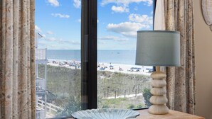 Een kamer met uitzicht op een strand, een tafel met een lamp en een raam met gordijnen.