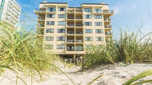 Een strandhotel met meerdere verdiepingen, omgeven door zand en duinriet.