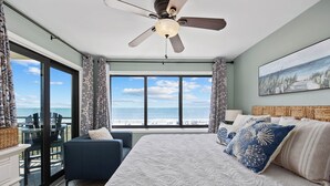 Een slaapkamer met een groot bed, een plafondventilator en uitzicht op het strand door grote ramen.