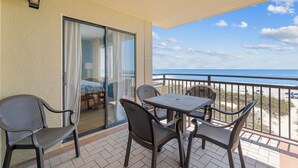 Un balcon avec une table et des chaises, une porte-fenêtre coulissante et une vue sur la plage et l’océan.