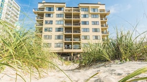 Un hôtel en bord de mer, avec plusieurs étages, entouré de sable et de végétation côtière.