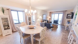 Un salón amplio con comedor, ventanas grandes, una araña y un televisor.