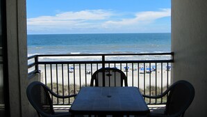 A balcony with a table and chairs overlooking a beach with umbrellas and people. - Oceanfront-402-- 3 Bedroom / 2 Bath Condo pet friendly in North Myrtle Beach (North Myrtle Beach)