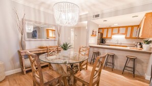 A modern kitchen with wooden cabinets, a glass dining table, and bar stools. - Oceanfront-402-- 3 Bedroom / 2 Bath Condo pet friendly in North Myrtle Beach (North Myrtle Beach)