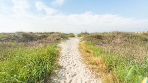 Uma trilha de areia serpenteia por uma área gramada sob um céu limpo.