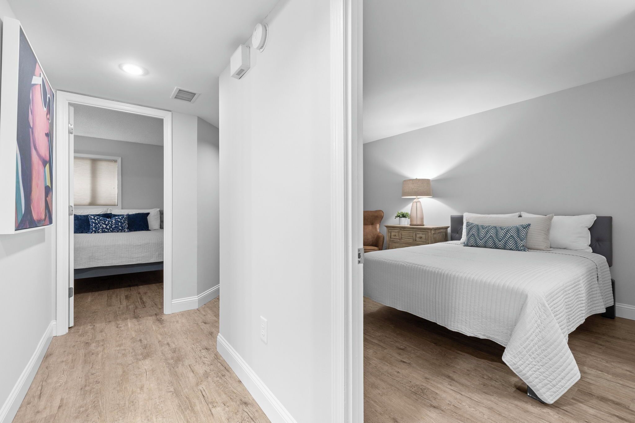 Un dormitorio con cama, mesita de noche, lámpara y una puerta que da a otra habitación.