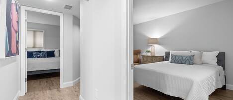 Un dormitorio con cama, mesita de noche, lámpara y una puerta que da a otra habitación.