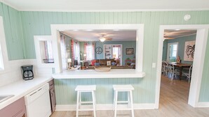 Una cocina con mostrador blanco, dos taburetes blancos y una zona de comedor con mesa y sillas.