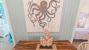 Una mesa de comedor de madera con sillas blancas, un centro de mesa decorativo y un cuadro de un pulpo.