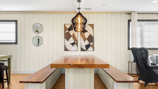A dining area with a wooden table and benches, a hanging pendant light, and two wall-mounted mirrors. - Close To Ocean Pet Friendly 6 Bedroom / 5 Bath Private Home with Private Pool (North Myrtle Beach)