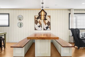 Un comedor con mesa de madera y bancos, una lámpara colgante y dos espejos en la pared.