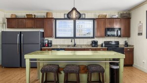 A kitchen with wooden cabinets, a central island with stools, a refrigerator, a microwave, and a window with blinds. - Close To Ocean Pet Friendly 6 Bedroom / 5 Bath Private Home with Private Pool (North Myrtle Beach)