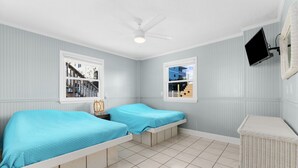 Une chambre avec deux lits, un ventilateur de plafond, une télévision et une vue sur l’extérieur.