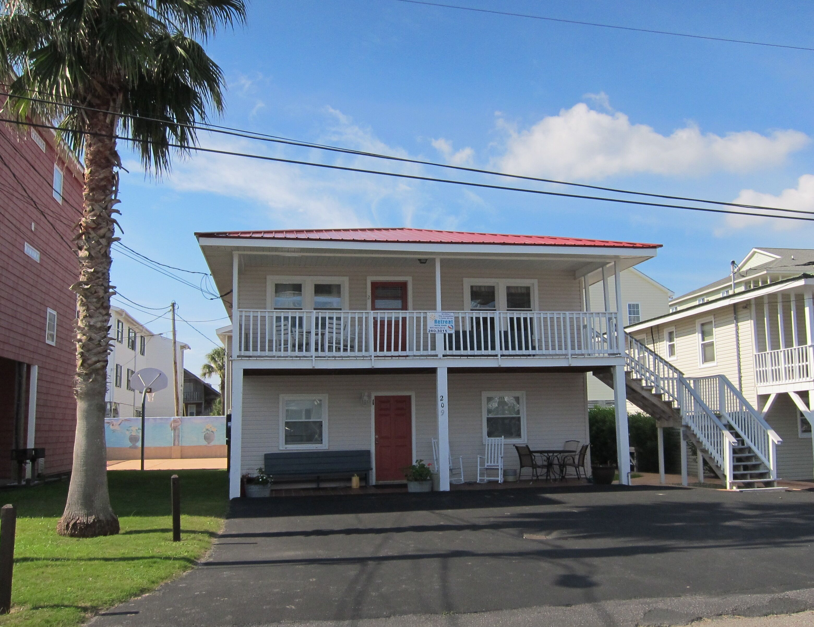 A two-story building with a balcony, a red door, and a staircase leading to the upper floor.