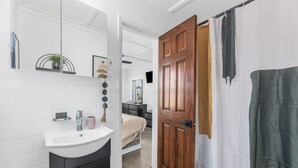 Une salle de bain avec un lavabo blanc, des meubles noirs, une porte en bois et un rideau de douche.
