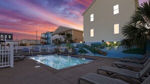 Une piscine avec des chaises longues, une fresque murale et une clôture portant une pancarte.