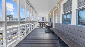 Un espace extérieur abrité doté d’une terrasse en bois, de rampes blanches et d’un coin salon avec des tables et des chaises.