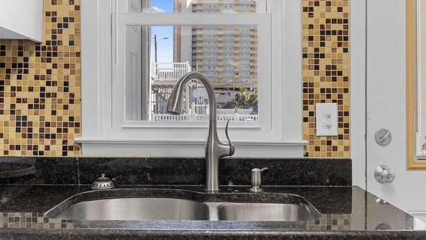 A kitchen with a double sink, a window with a view of a building, and a tiled backsplash. - Short walk to Beach, 2 Bedroom/1 Bath Quad 2 (down) pool access near Main St (North Myrtle Beach)