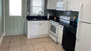A kitchen with white cabinets, a black countertop, a stove, an oven, a microwave, and a refrigerator. - Short walk to Beach, 2 Bedroom/1 Bath Quad 3 (up) w/pool access near Main St (North Myrtle Beach)