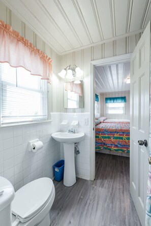 Une petite salle de bain comprenant des toilettes, un lavabo et une fenêtre avec des stores.