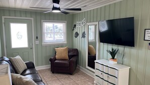 A living room with a dark leather sofa, a white cabinet, a ceiling fan, a television, and a door with a window. - Short walk to Beach, 2 Bedroom/1 Bath Quad 3 (up) w/pool access near Main St (North Myrtle Beach)