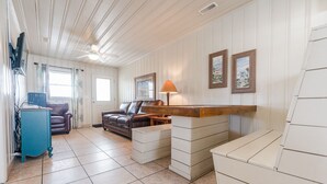 A living room with a brown leather sofa, a white coffee table, and a blue cabinet. There are two framed pictures on the wall and a lamp on the coffee table. - Short walk to Beach, 2 Bedroom/1 Bath Quad 4 (up) w/pool access near Main St (North Myrtle Beach)