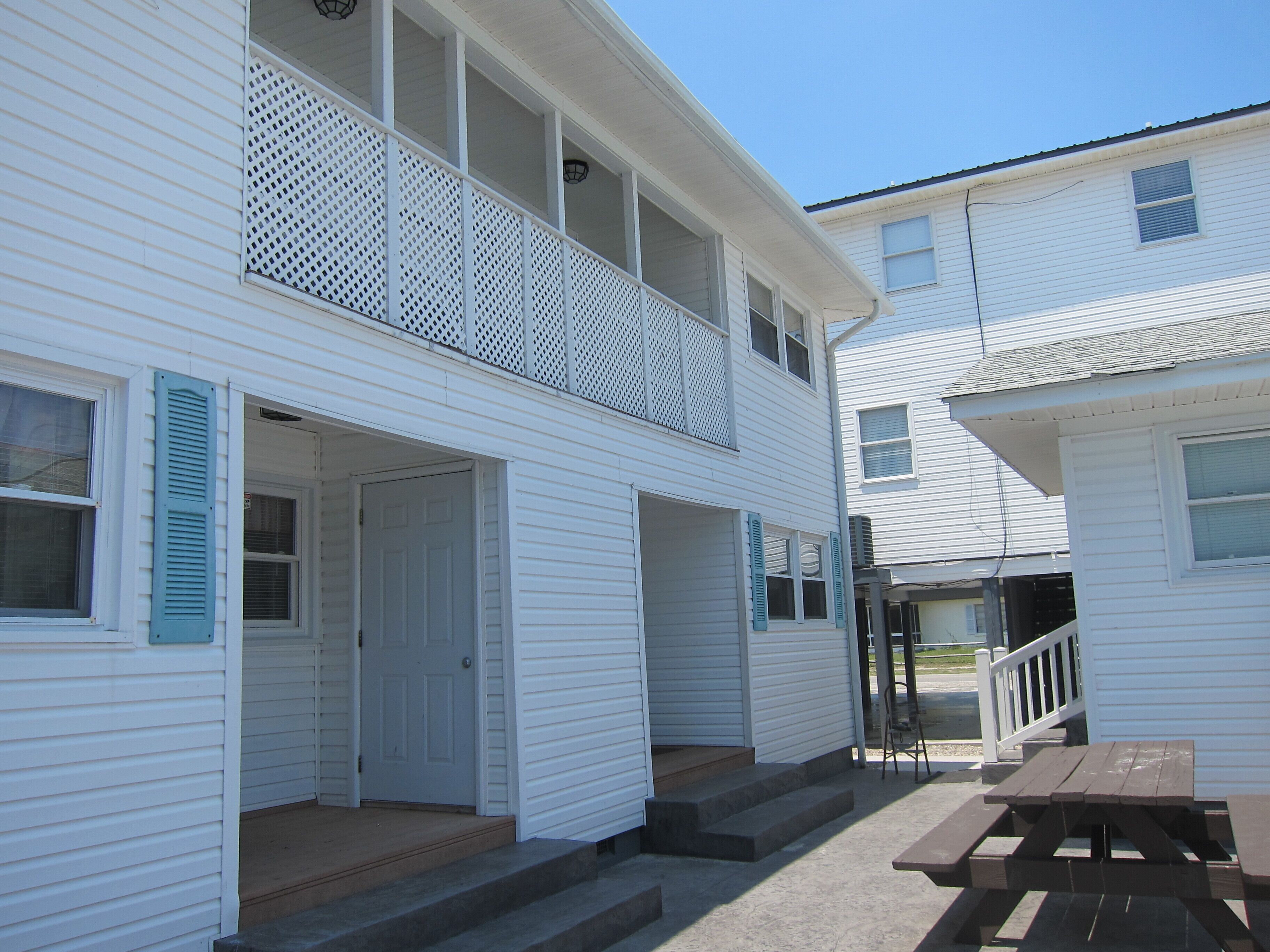 A two-story white building with a balcony, a front door, and a wooden bench.