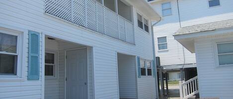 A two-story white building with a balcony, a front door, and a wooden bench.